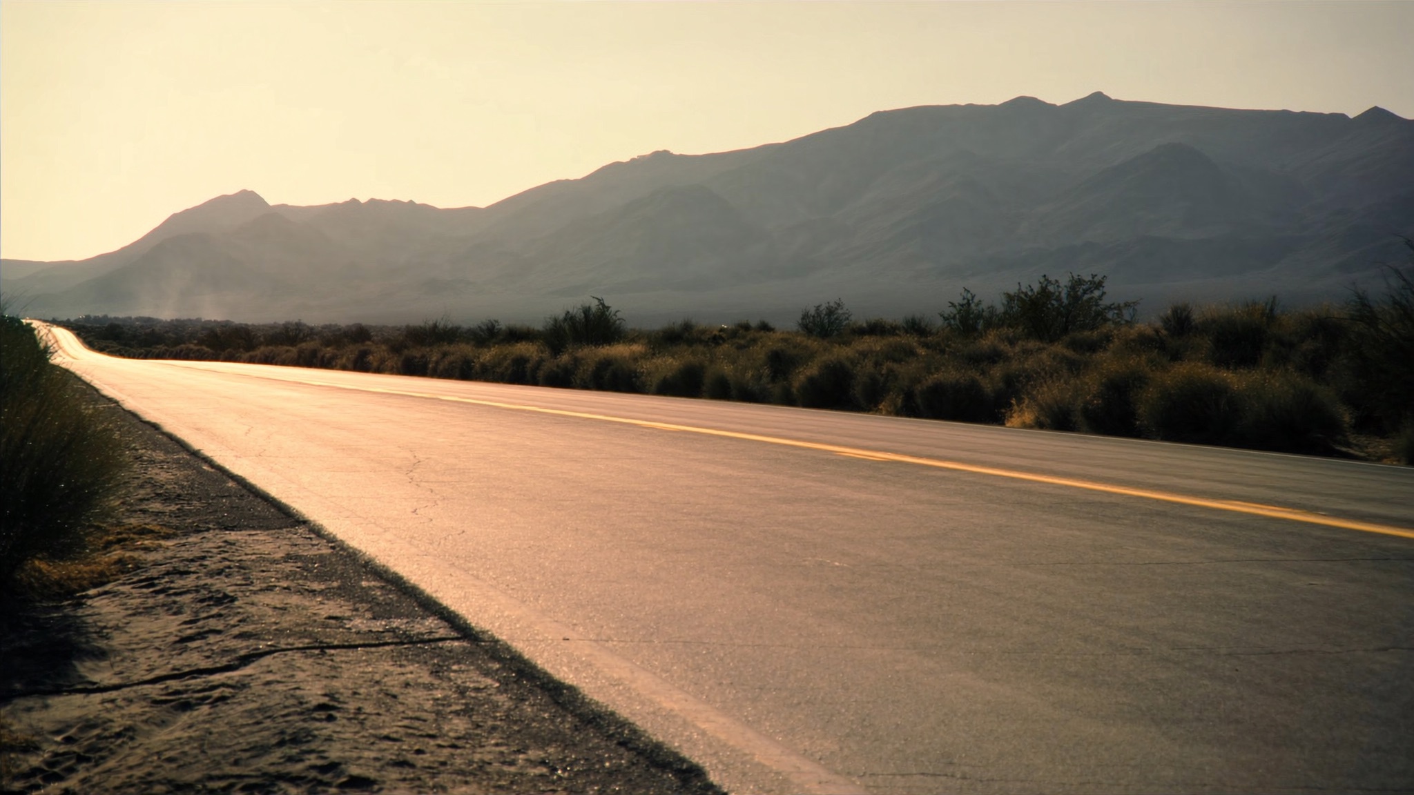 Empty desert road at golden hour running toward distant mountains.