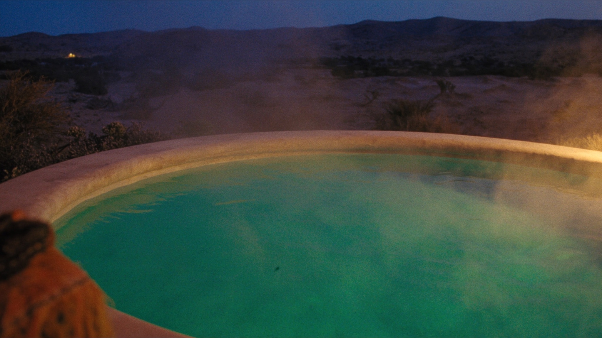Warm mineral soaking pool at blue hour with rising steam and a travertine edge.