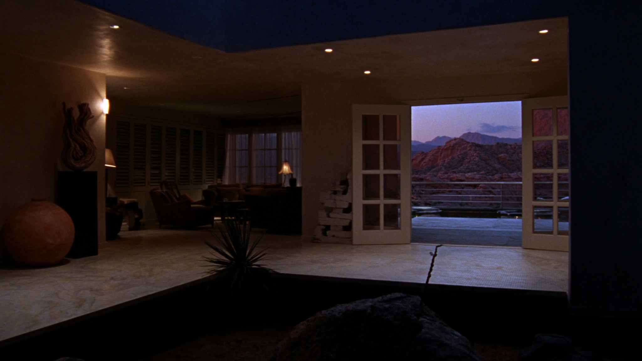 Warm desert villa interior at dusk with open doors onto a glowing mineral pool.